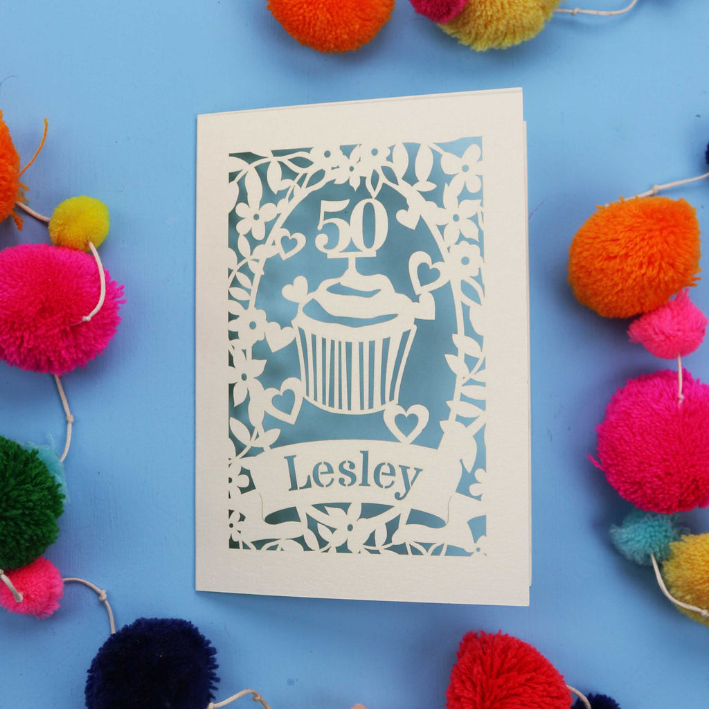 A 50th birthday Card with '50' and 'Lesley' on a blue background with colourful pom-poms