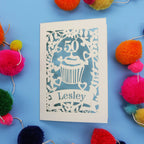 A 50th birthday Card with '50' and 'Lesley' on a blue background with colourful pom-poms