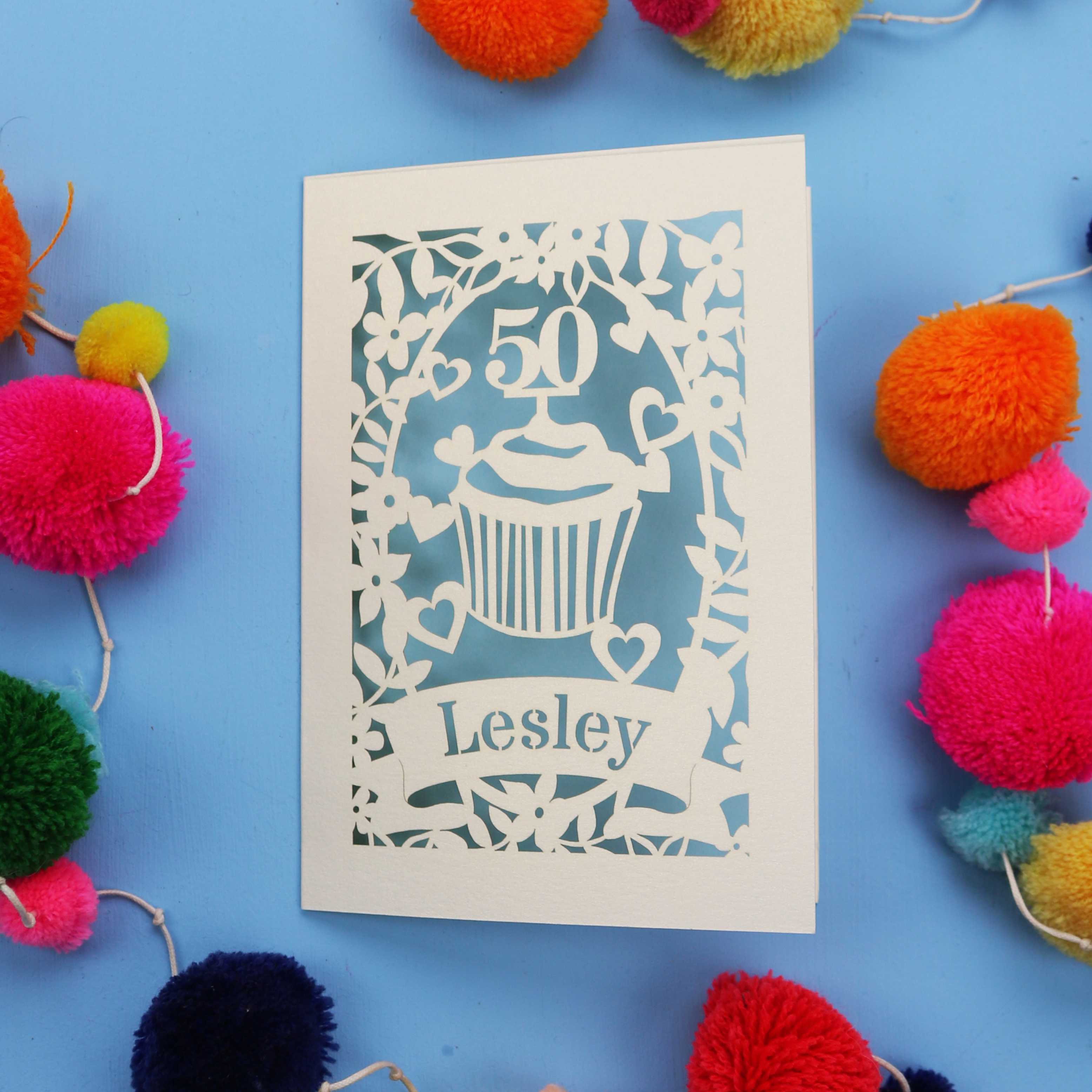 A 50th birthday Card with '50' and 'Lesley' on a blue background with colourful pom-poms