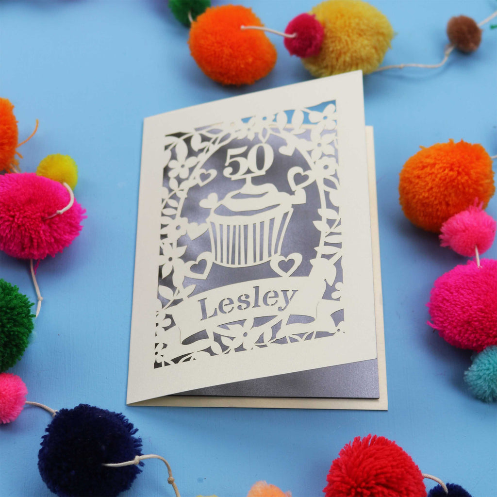A 50th birthday Card with '50' and 'Lesley' on a blue background with colourful pom-poms