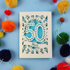 A personalised 50th Birthday Card with '50' laser cut design on a blue background with colourful pom-poms.
