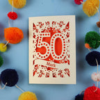 A personalised 50th Birthday Card for him, with '50' laser cut design on a blue background with colourful pom-poms.