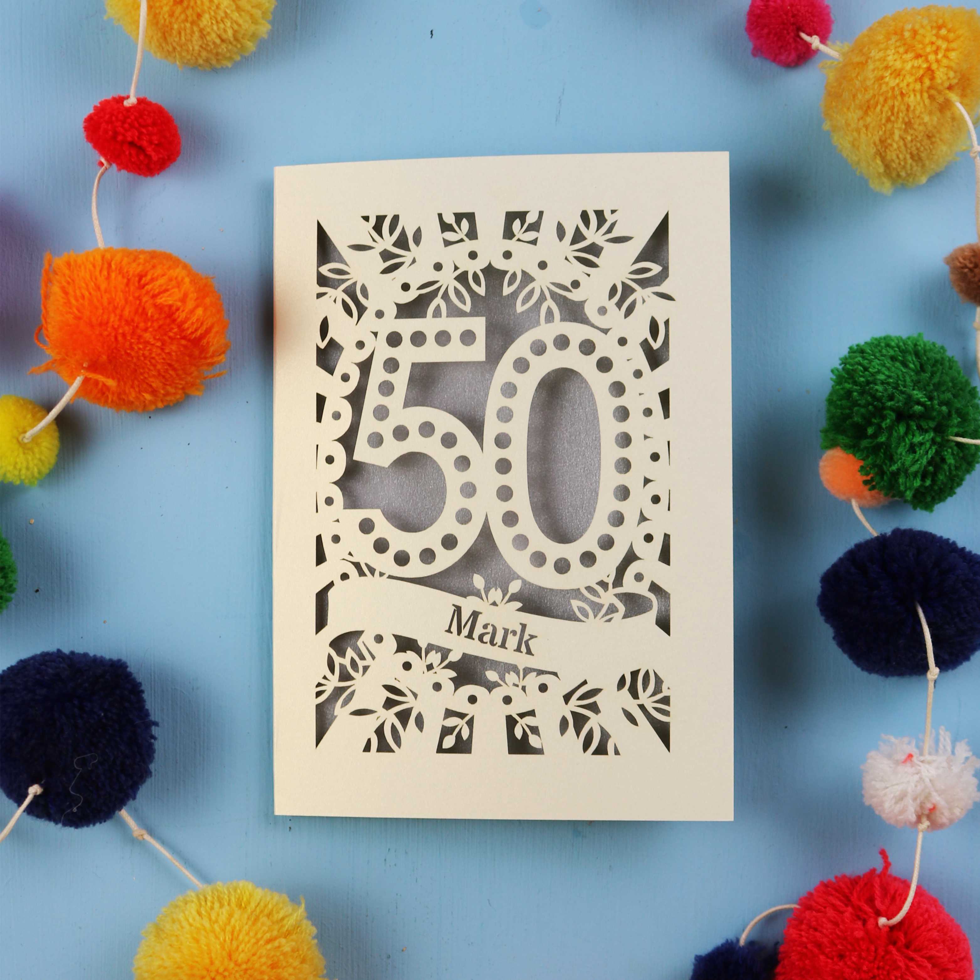 50th Birthday Card with a spotty '50' laser cut design on a blue background with colourful pom-poms.