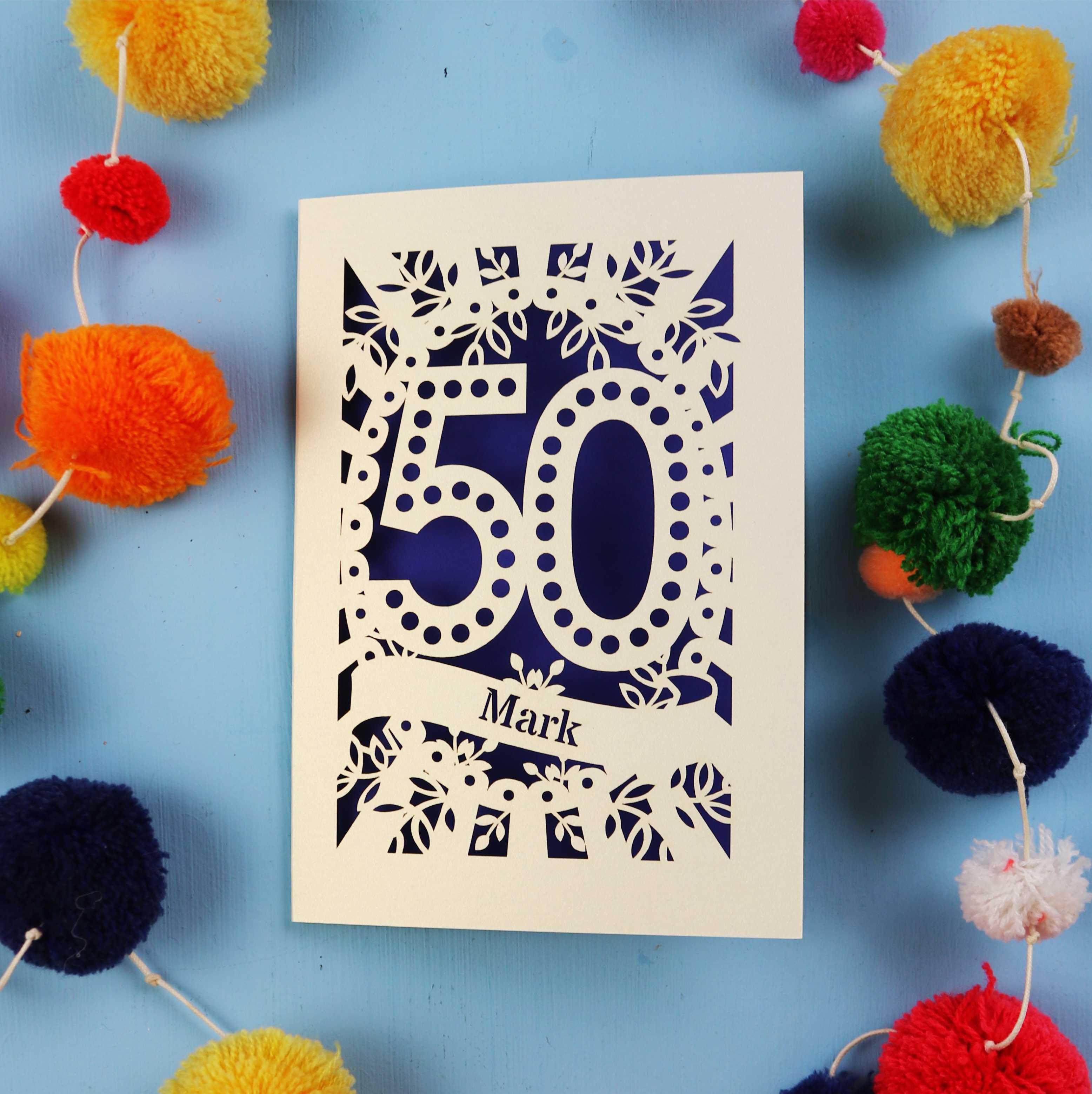 Personalised laser cut 50th Birthday Card with '50' laser cut design on a blue background with colourful pom-poms.