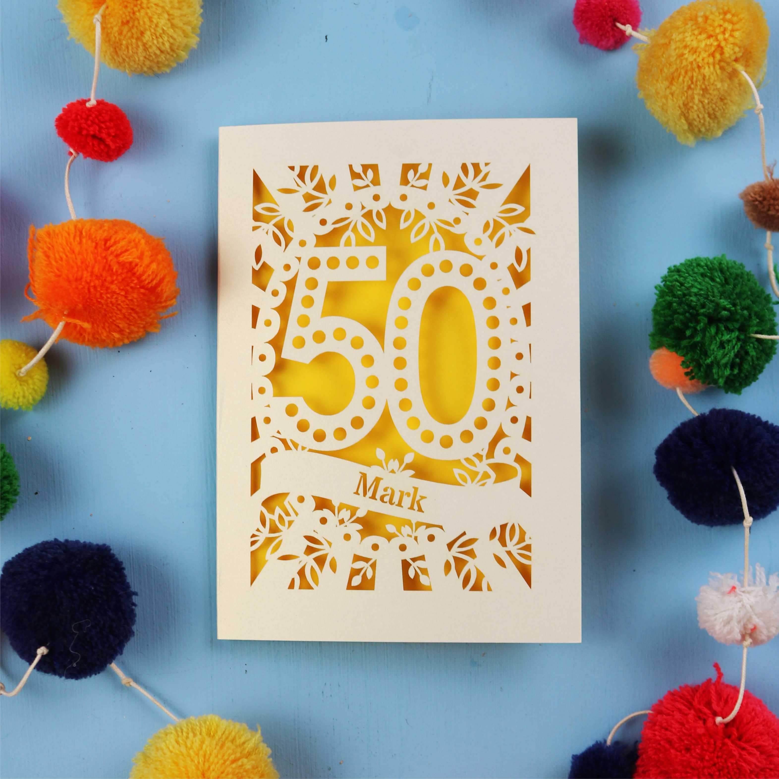 50th Birthday Card with '50' laser cut design on a blue background with colourful pom-poms.