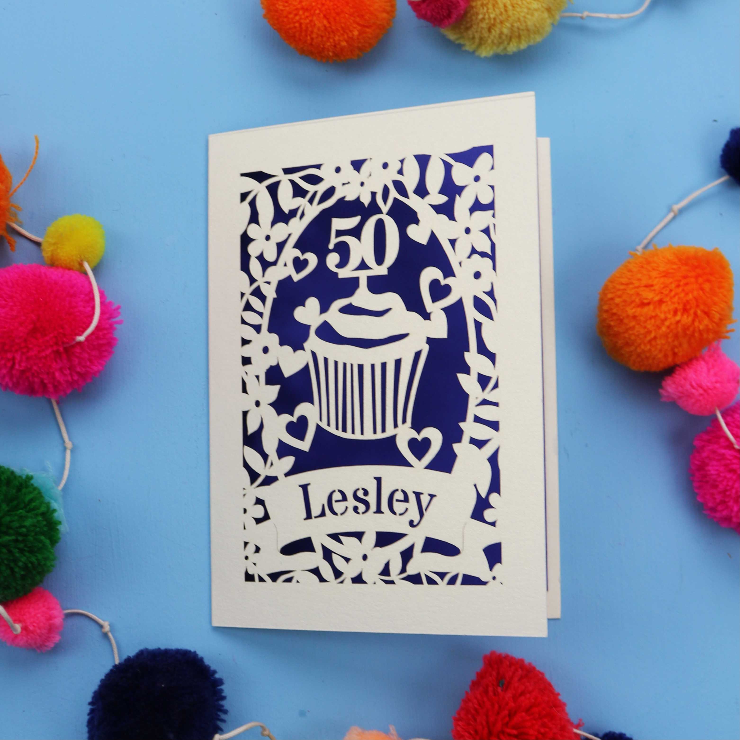 A 50th birthday Card with '50' and 'Lesley' on a blue background with colourful pom-poms