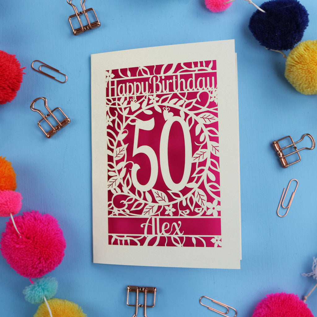 Birthday card with 'Happy Birthday 50 Alex' on a blue background with colourful pom-poms and paper clips.