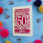 Birthday card with 'Happy Birthday 50 Alex' on a blue background with colourful pom-poms and paper clips.