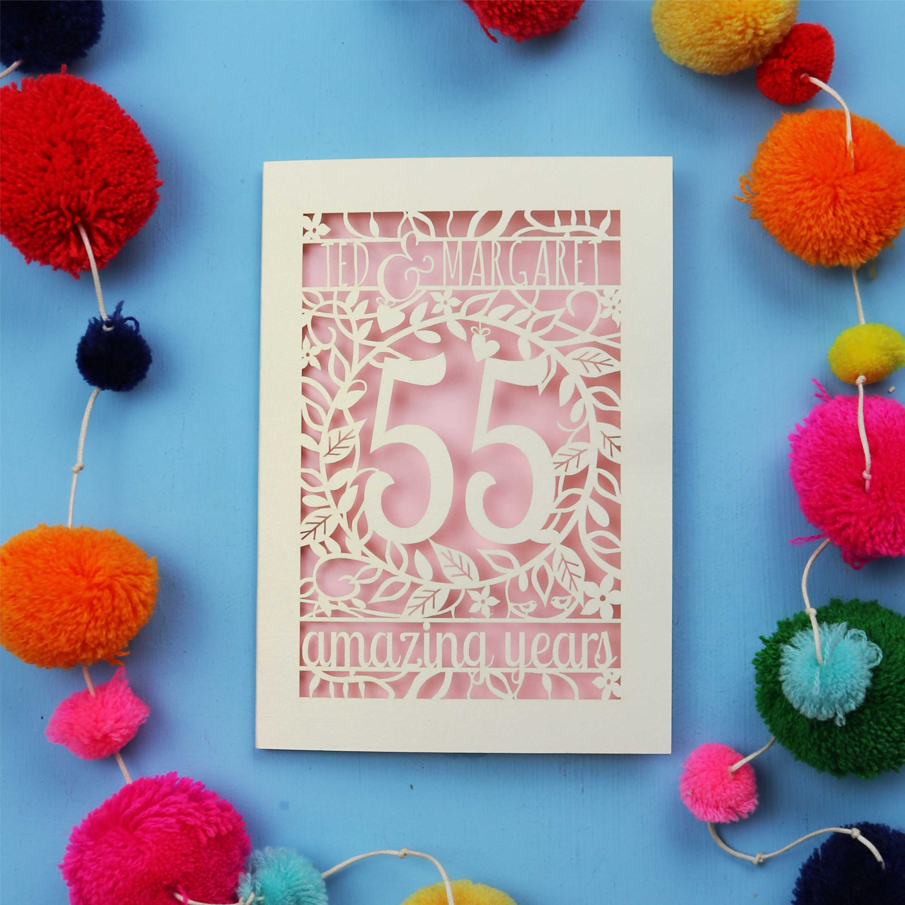 Cut out Emerald anniversary Card with '55 amazing years' design on a blue background with colourful pom-poms.
