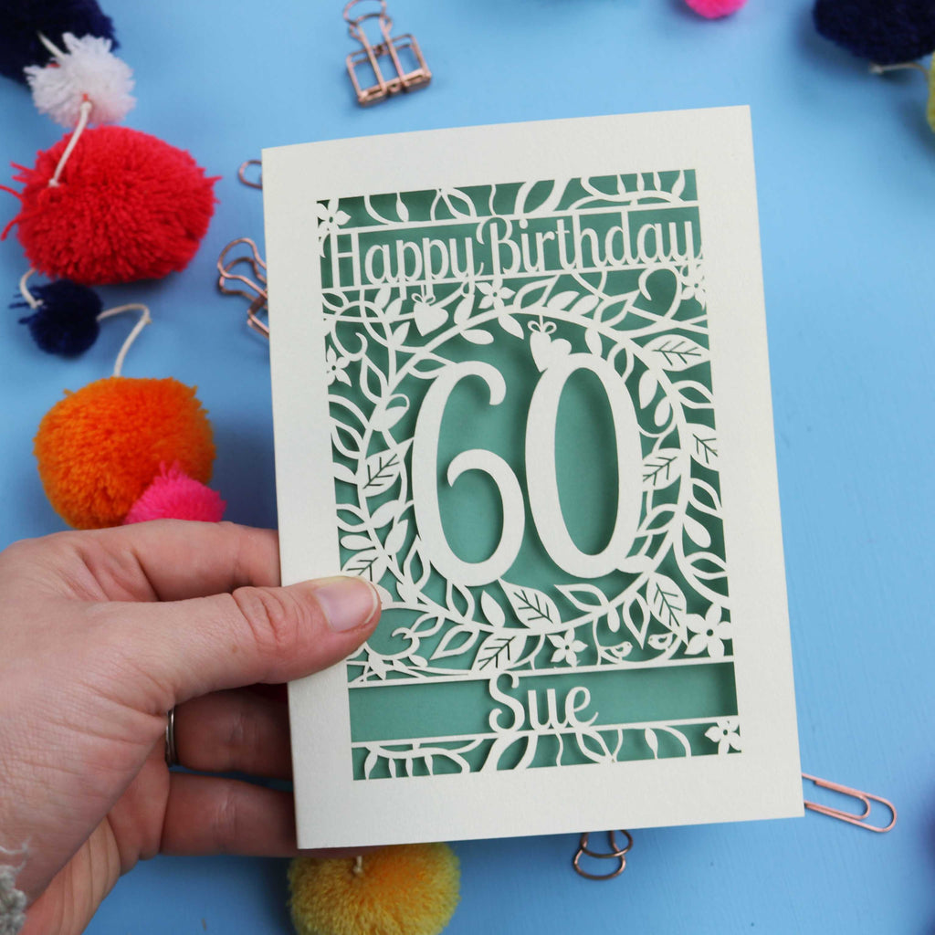 Personalised 60th Birthday card with 'Happy Birthday 60 Sue' on a blue background with colourful pom-poms and paper clips.