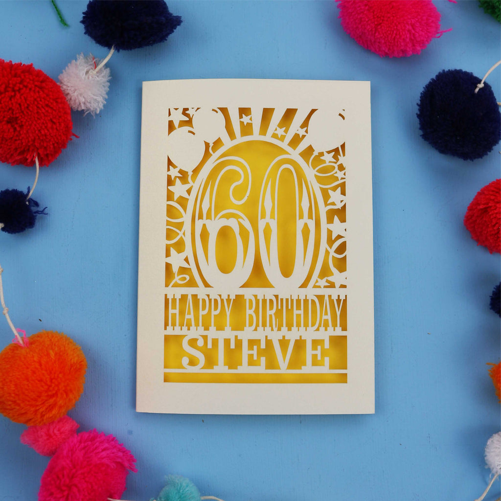 Birthday card with '60th Happy Birthday Steve' on a blue background with colorful pom-poms.