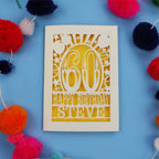 Birthday card with '60th Happy Birthday Steve' on a blue background with colorful pom-poms.