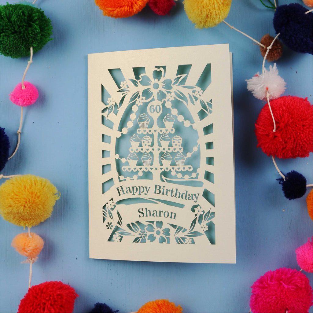 Laser Cut 60th Birthday card with personalized name surrounded by colourful pom-poms on a blue background