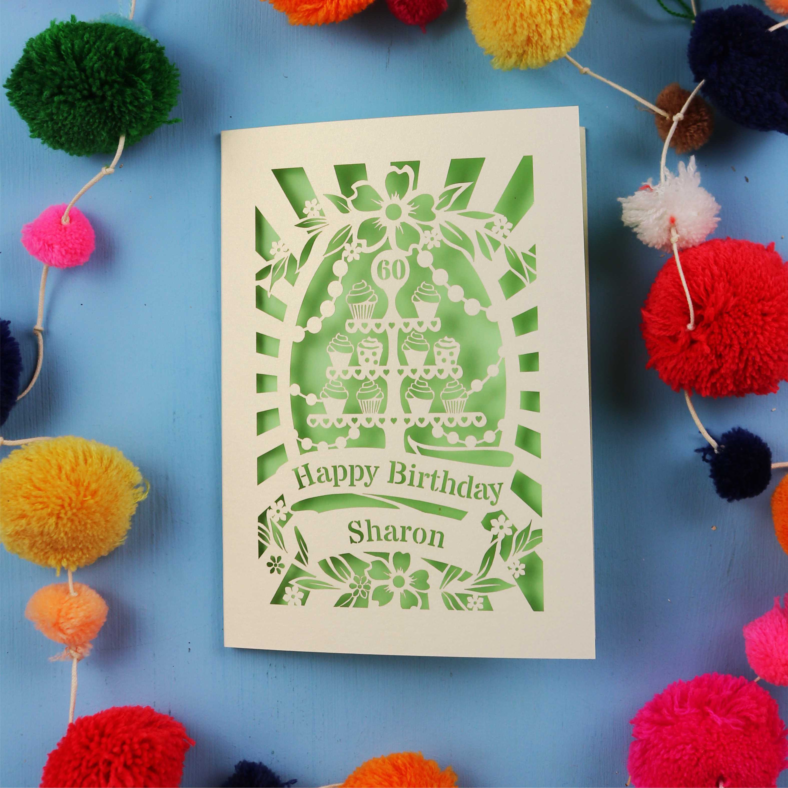 Laser Cut 60th Birthday card with personalized name surrounded by colourful pom-poms on a blue background