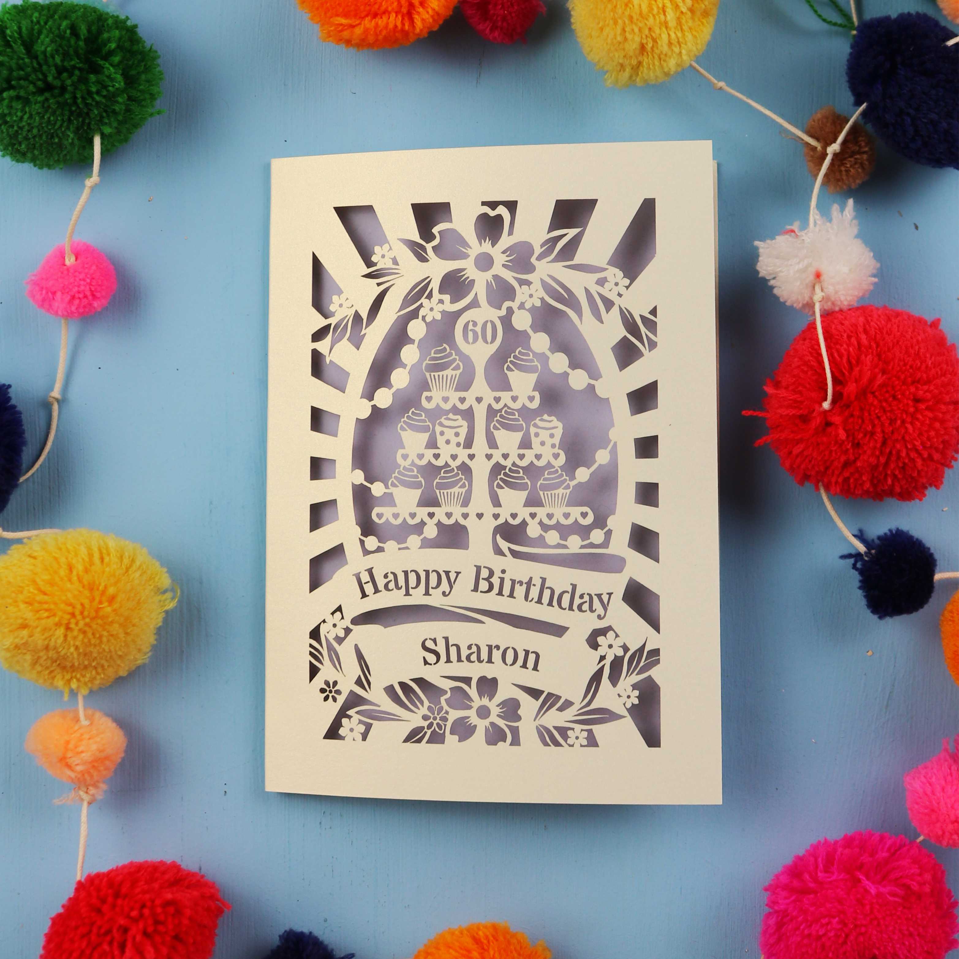 Laser Cut 60th Birthday card with personalized name surrounded by colourful pom-poms on a blue background