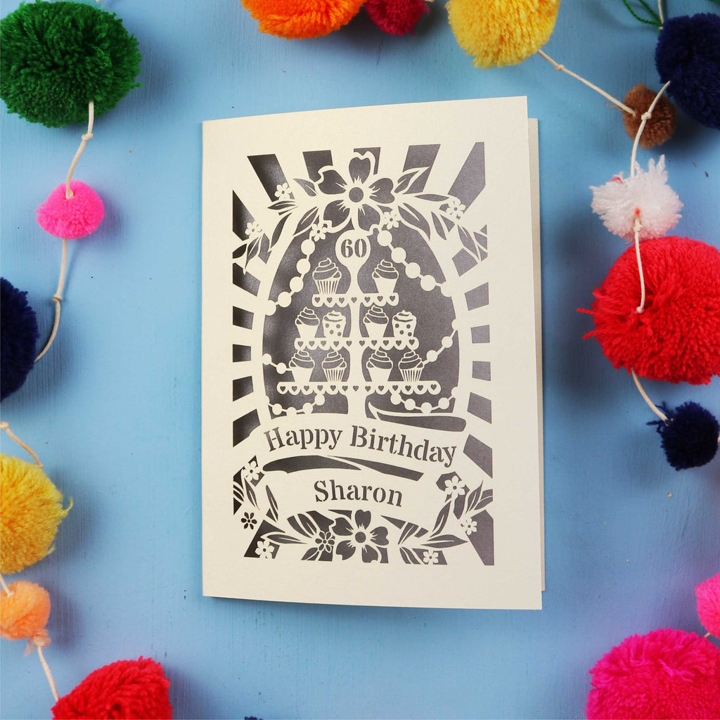 Laser Cut 60th Birthday card with personalized name surrounded by colourful pom-poms on a blue background