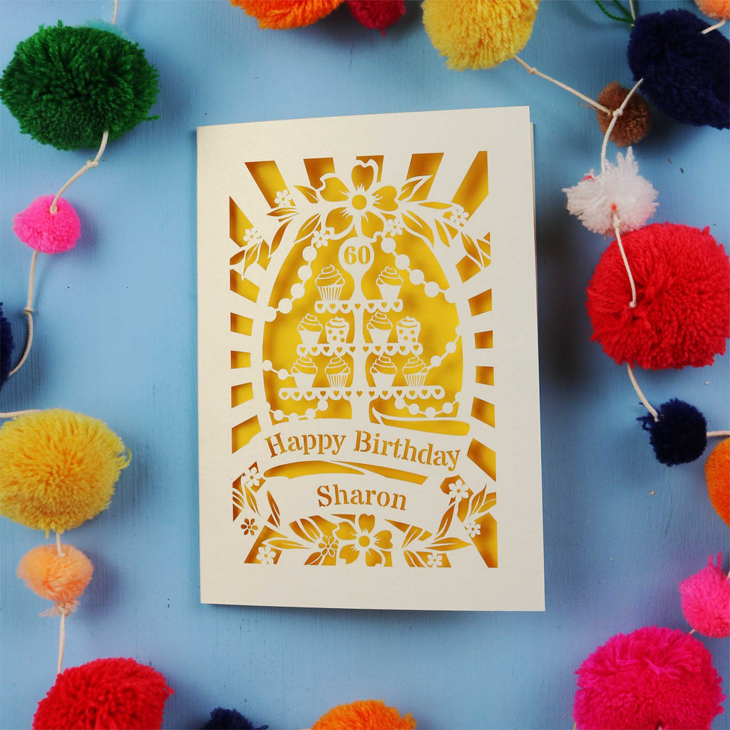Laser Cut 60th Birthday card with personalized name surrounded by colourful pom-poms on a blue background