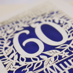 A laser cut 60th birthday card with cut out floral border and "Happy Birthday" with a number 60 in the centre 