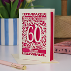 A laser cut 60th birthday card with cut out floral border and "Happy Birthday" with a number 60 in the centre and personalised at the bottom with a name. 