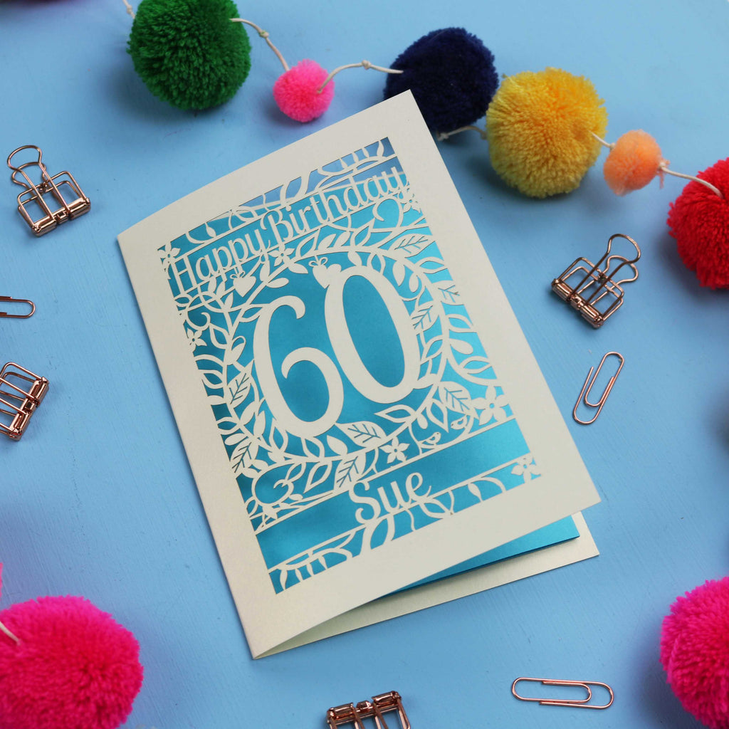 Laser cut 60th Birthday card with 'Happy Birthday 60 Sue' on a blue background with colourful pom-poms and paper clips.