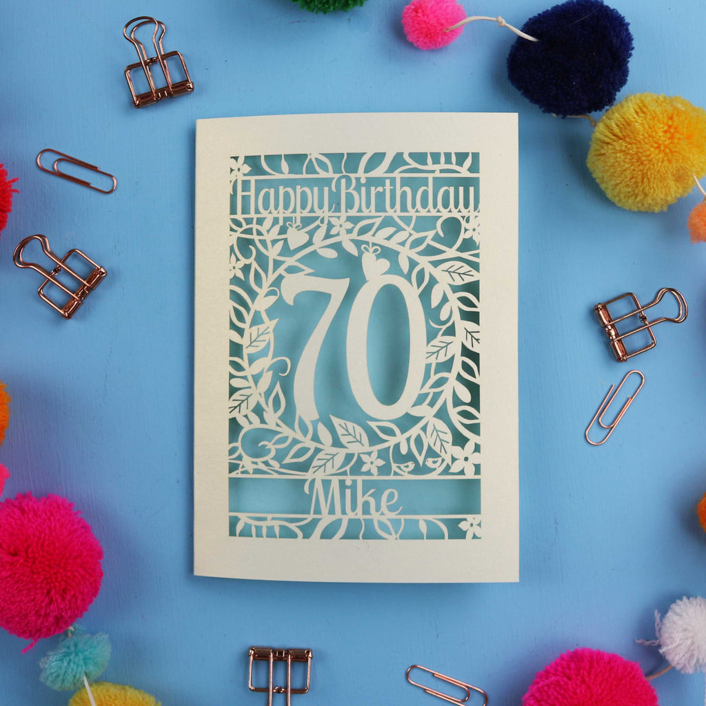 A paper cut 70th birthday card with 'Happy Birthday' and personalised with the recipient's name. The number 70 is in the centre, surrounded by leaf and floral cut out designs. 