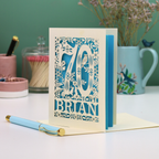 Luxury 70th birthday card with floral  woodland design and '70' 'Brian' text on a table.