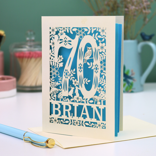 Decorative 70th birthday card with floral  woodland design and '70' 'Brian' text on a table.