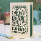 Laser cut 70th birthday card with floral  woodland design and '70' 'Brian' text on a table.