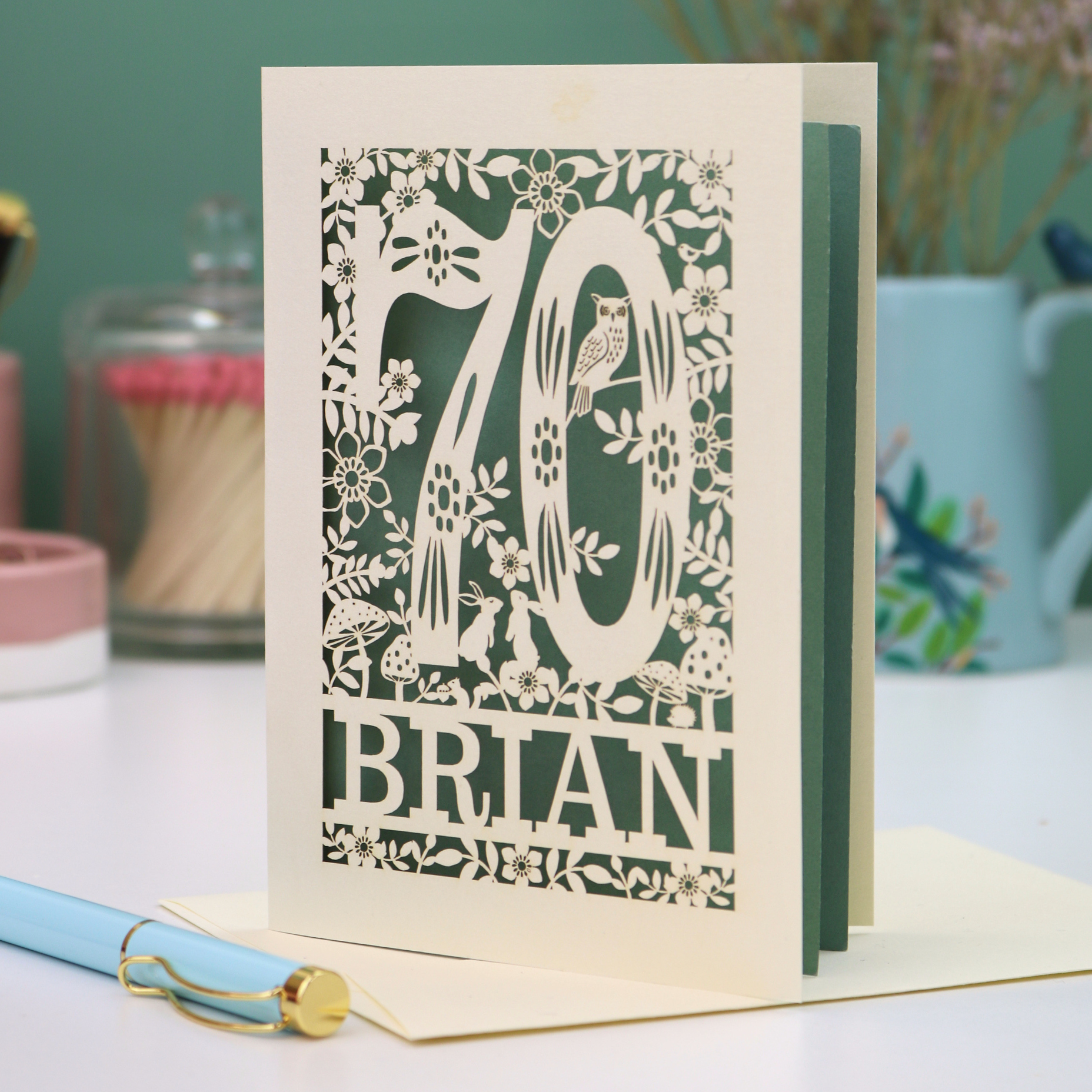 Laser cut 70th birthday card with floral  woodland design and '70' 'Brian' text on a table.