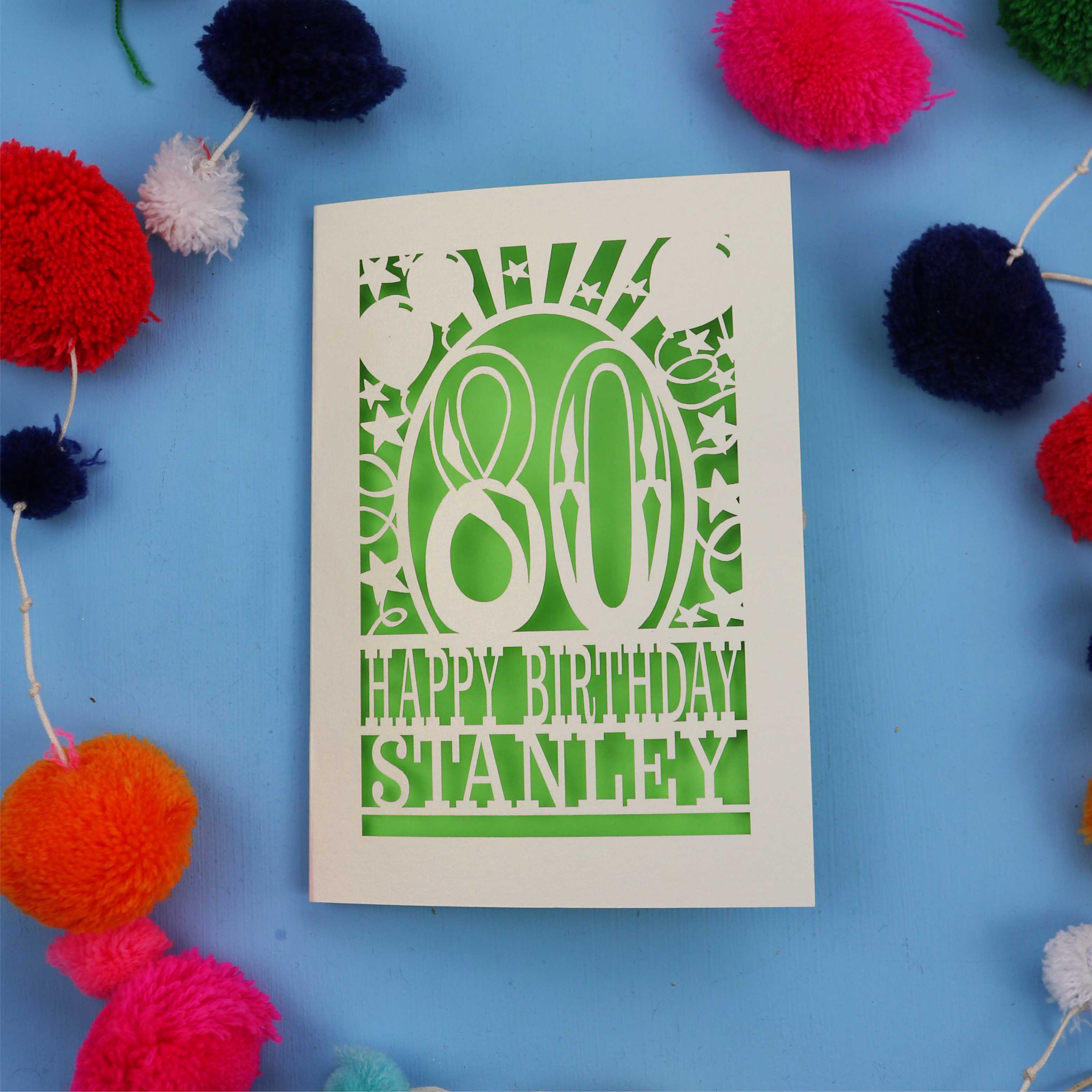 80th Birthday card with 'Happy Birthday Stanley' on a blue background with colourful pom-poms.