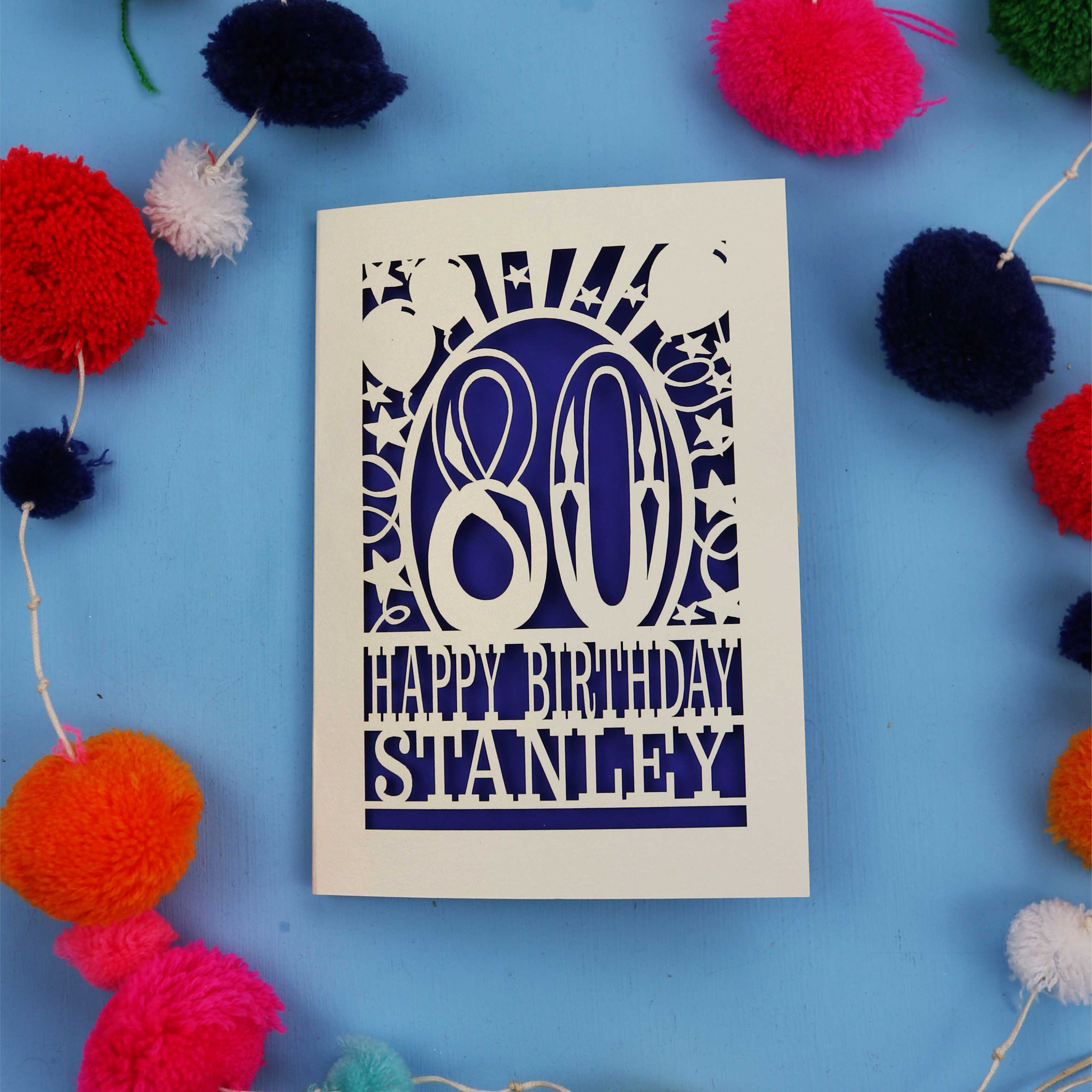 80th Birthday card with 'Happy Birthday Stanley' on a blue background with colourful pom-poms.