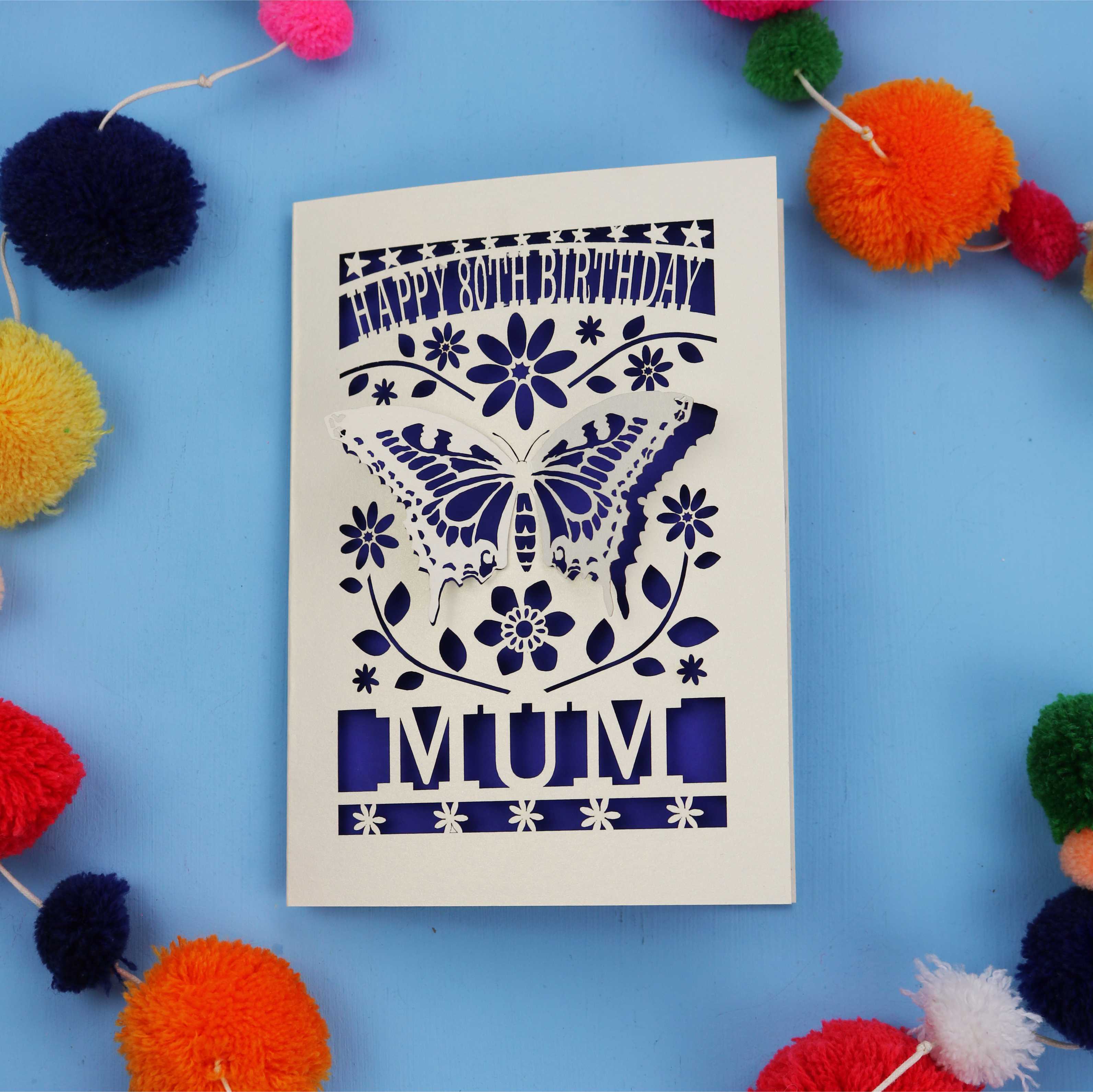 80th Birthday Card with butterfly design and 'Happy Birthday Mum' text on a blue background with colourful pom-poms.