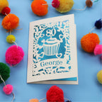 Personalised Laser cut 80th Birthday Card with '80' cut out cupcake design on a blue background with colourful pom-poms.