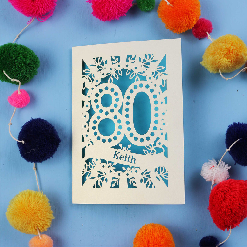 Keepsake 80th Birthday Card with '80' cut out design on a blue background with colourful pom-poms.