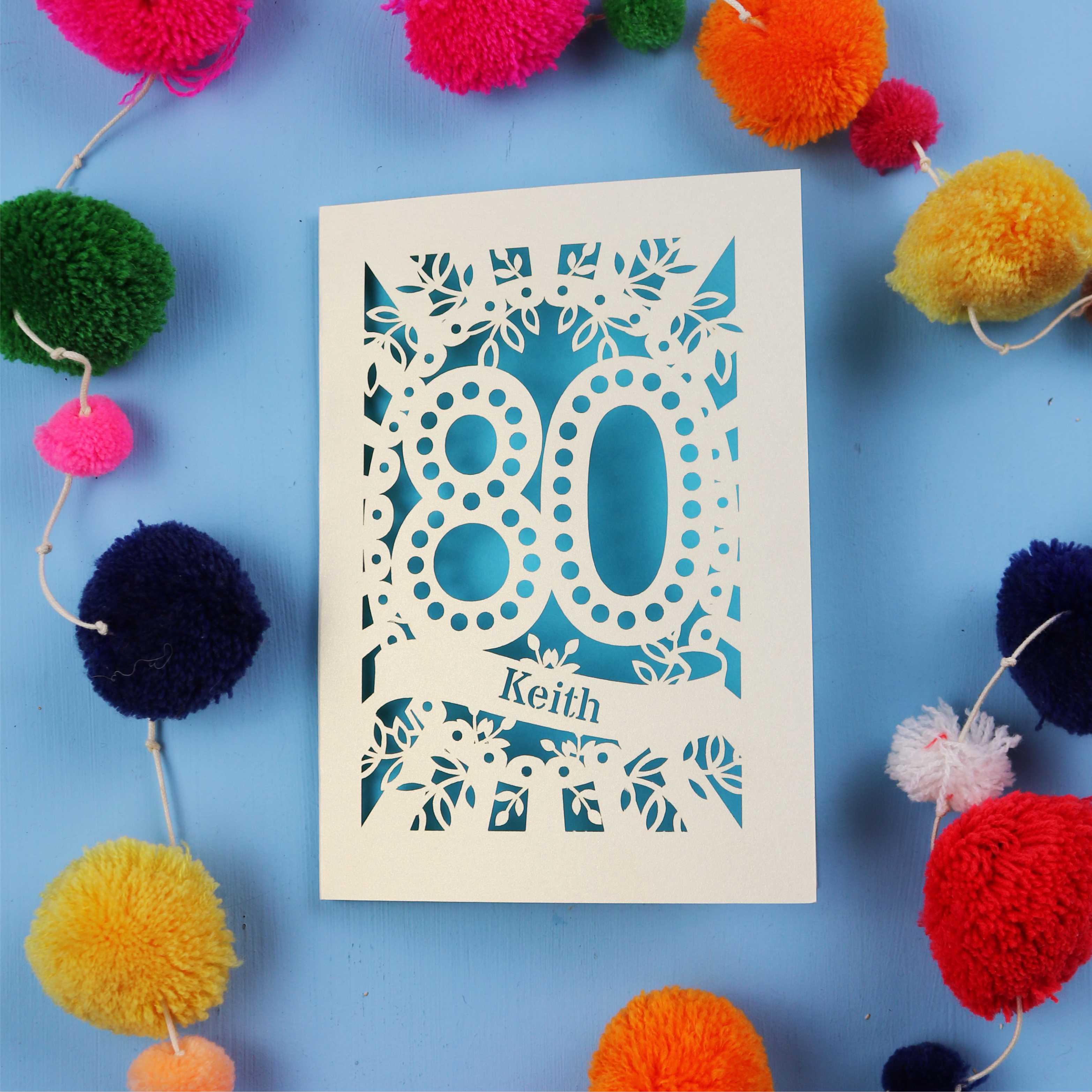 Keepsake 80th Birthday Card with '80' cut out design on a blue background with colourful pom-poms.