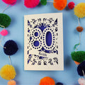 Laser cut 80th Birthday Card with '80' cut out design on a blue background with colourful pom-poms.