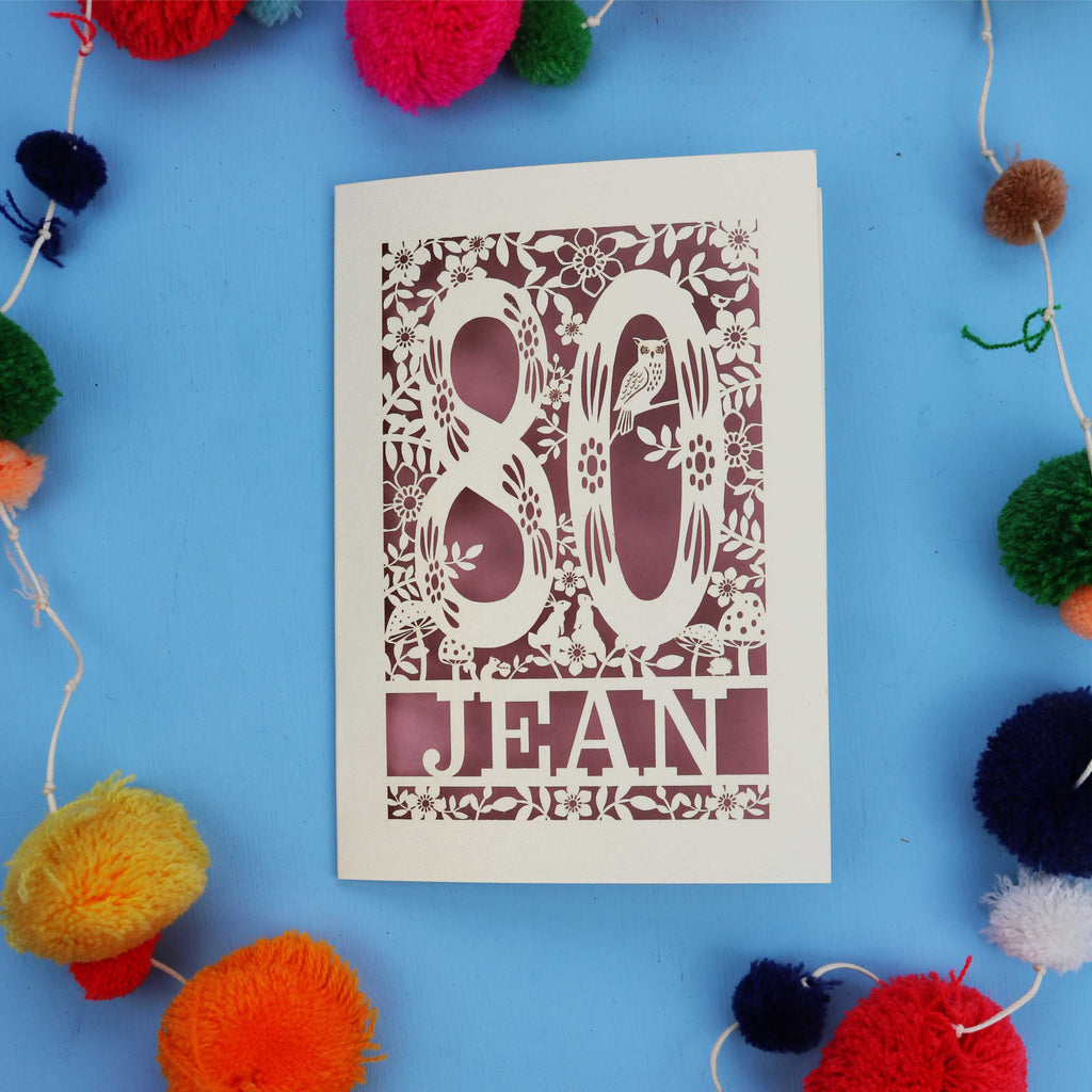 Decorative 80th Birthday card with '80 Jean' design on a blue background with colourful pom-poms.