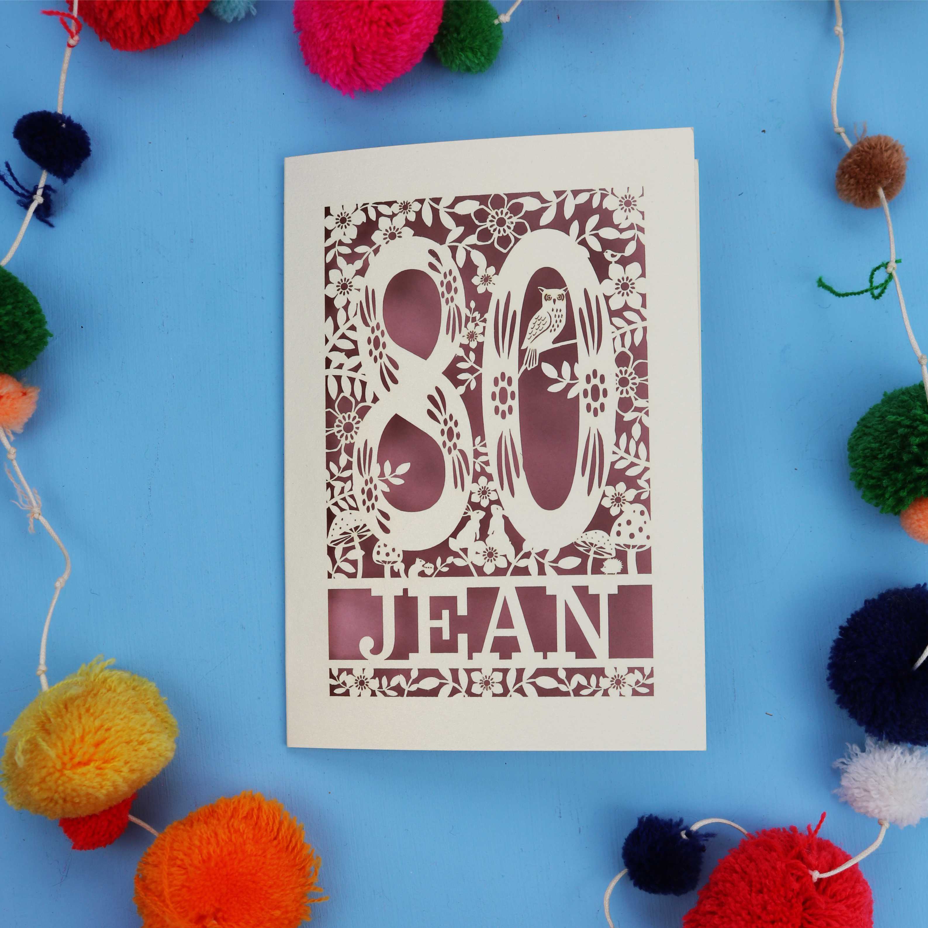 Decorative 80th Birthday card with '80 Jean' design on a blue background with colourful pom-poms.