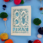 Unique 80th Birthday card with '80 Jean' design on a blue background with colourful pom-poms.