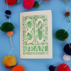 Beautiful 80th Birthday card with '80 Jean' design on a blue background with colourful pom-poms.