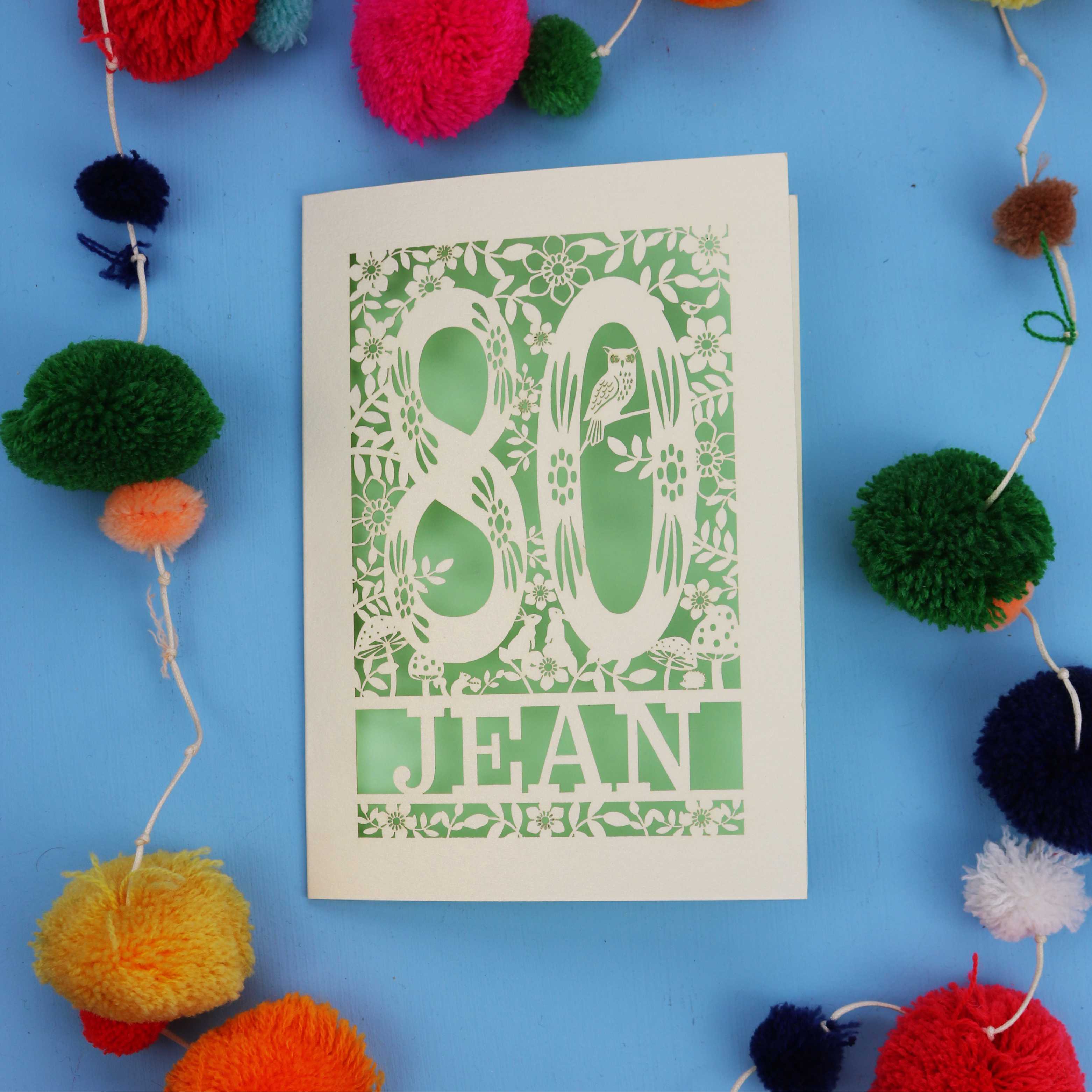 Beautiful 80th Birthday card with '80 Jean' design on a blue background with colourful pom-poms.
