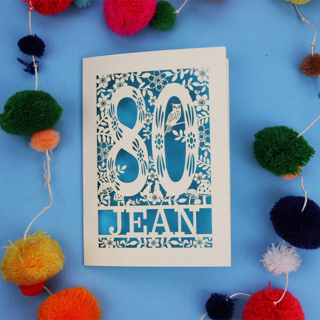 Keepsake 80th Birthday card with '80 Jean' design on a blue background with colourful pom-poms.