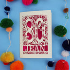 Personalised 80th Birthday card with '80 Jean' design on a blue background with colourful pom-poms.