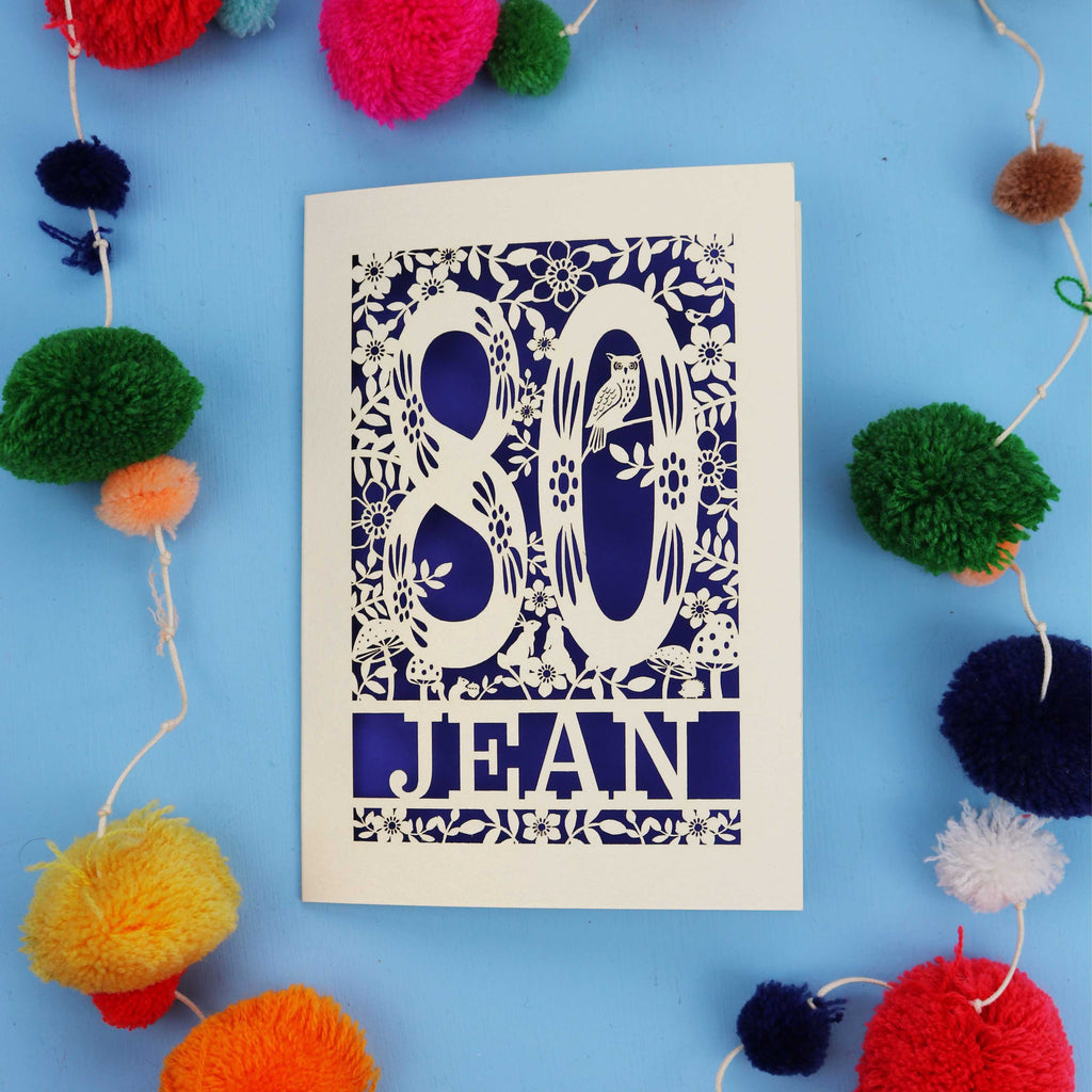 Woodland 80th Birthday card with '80 Jean' design on a blue background with colourful pom-poms.