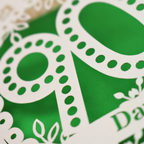 A close-up of a green and cream decorative paper cut out birthday card featuring large stylized numbers and leaf motifs