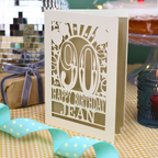 A laser cut 90th birthday card with balloons and stars around a decorative number '90', with personalised text 'Happy Birthday Jean'