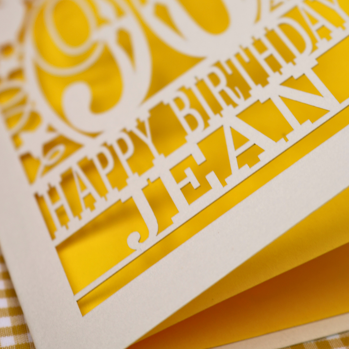 A close up of a laser cut 90th birthday card with balloons and stars around a decorative number '90', with personalised text 'Happy Birthday Jean' 