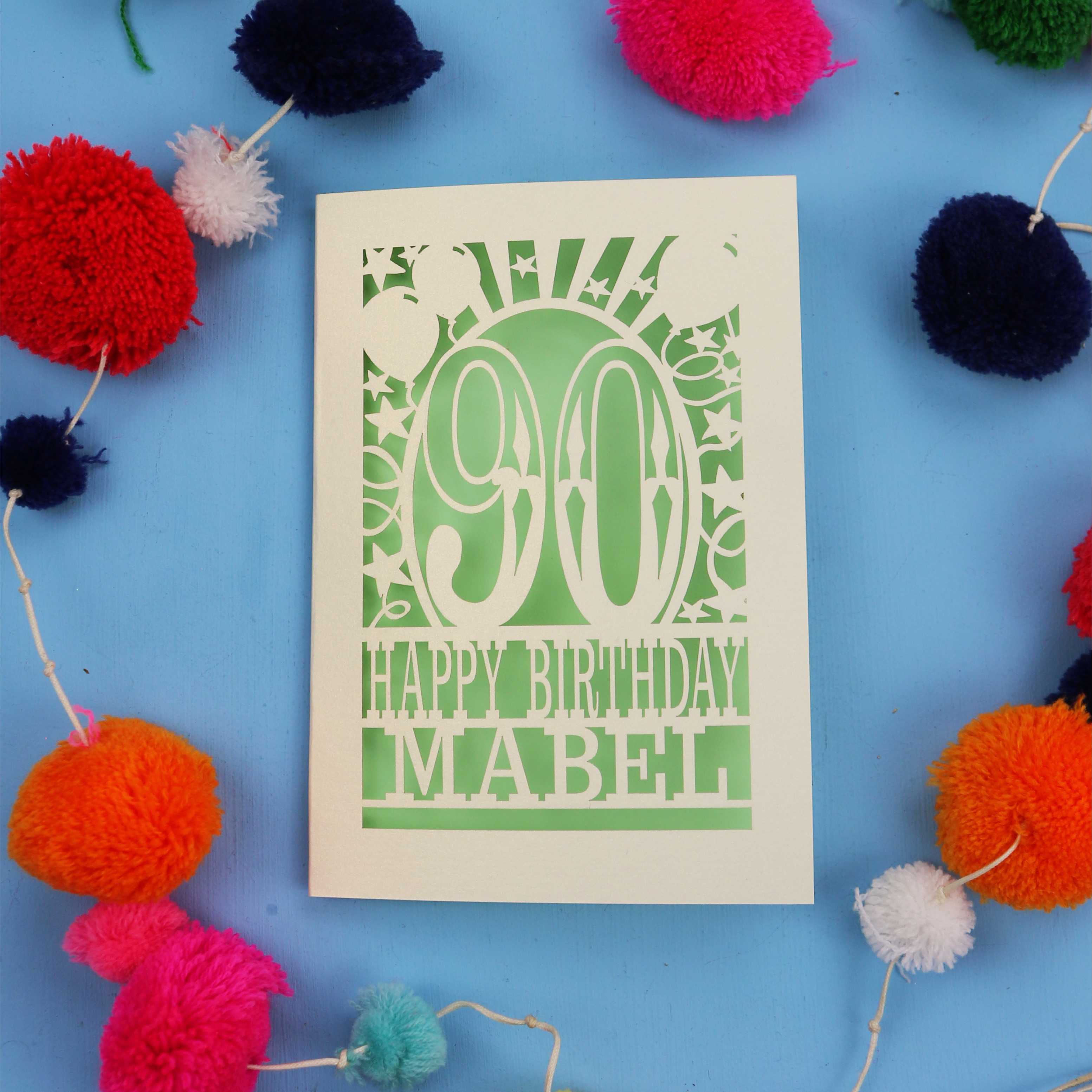 Happy Birthday Mabel - A personalised 90th birthday card with colourful pom-poms on a blue background