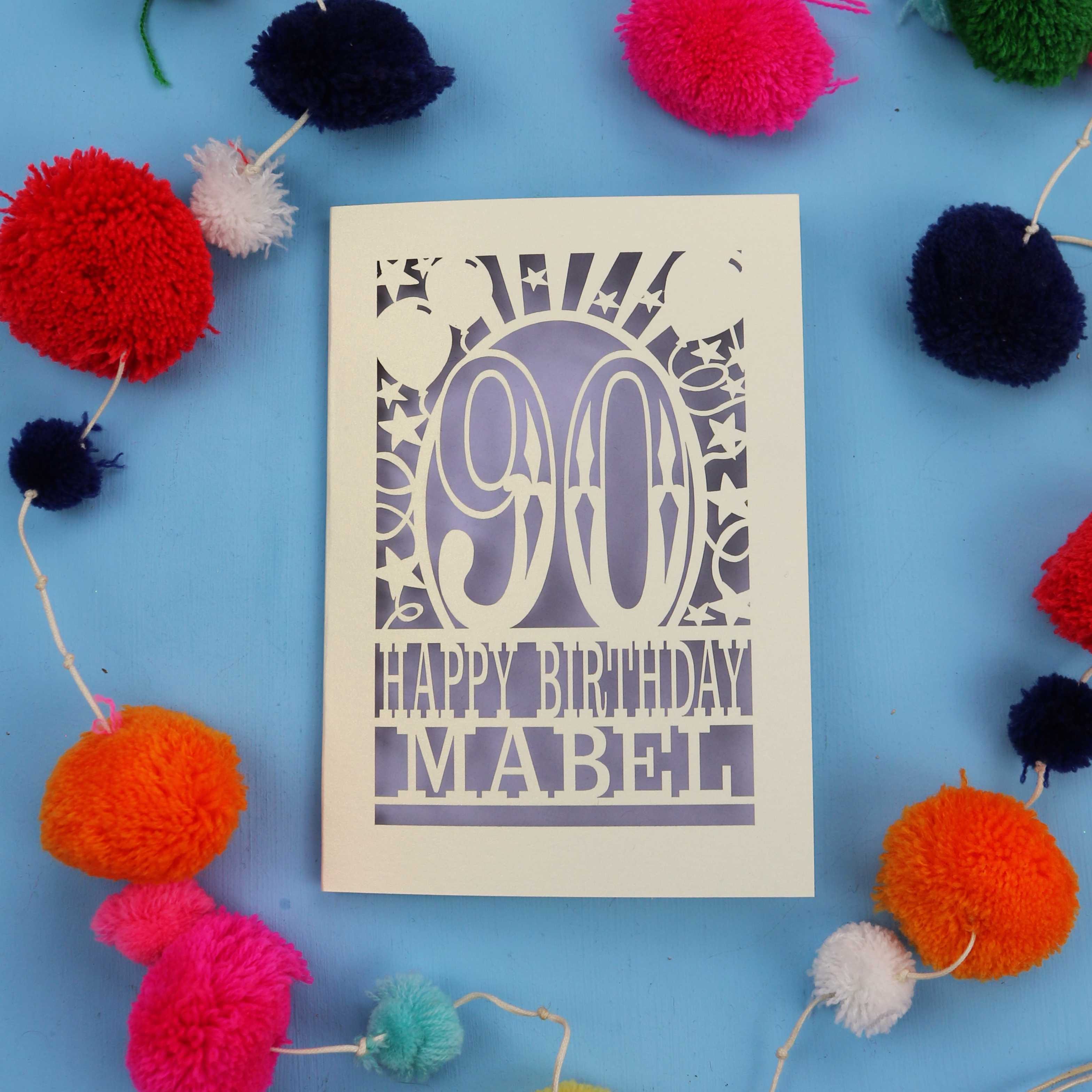 A personalised 90th birthday card with colourful pom-poms on a blue background