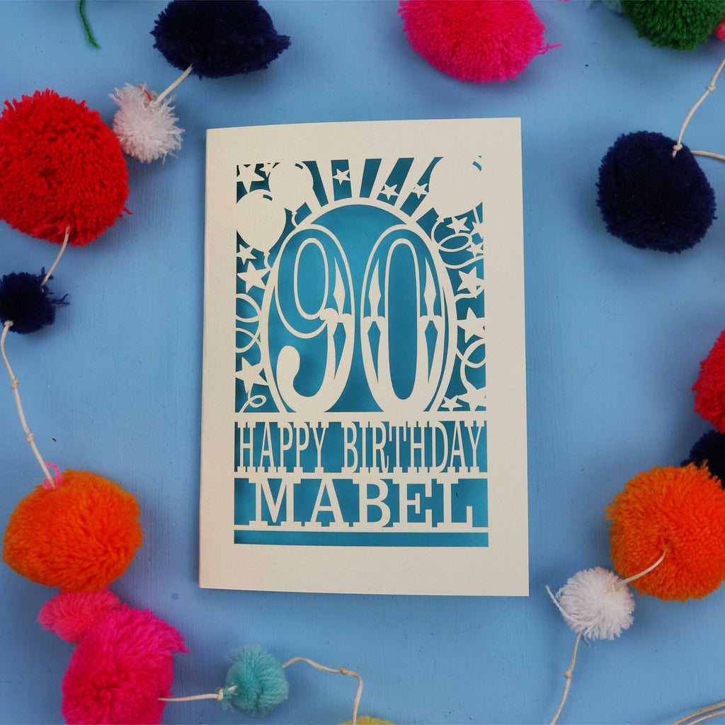 Happy Birthday Mabel - A personalised 90th birthday card with colourful pom-poms on a blue background